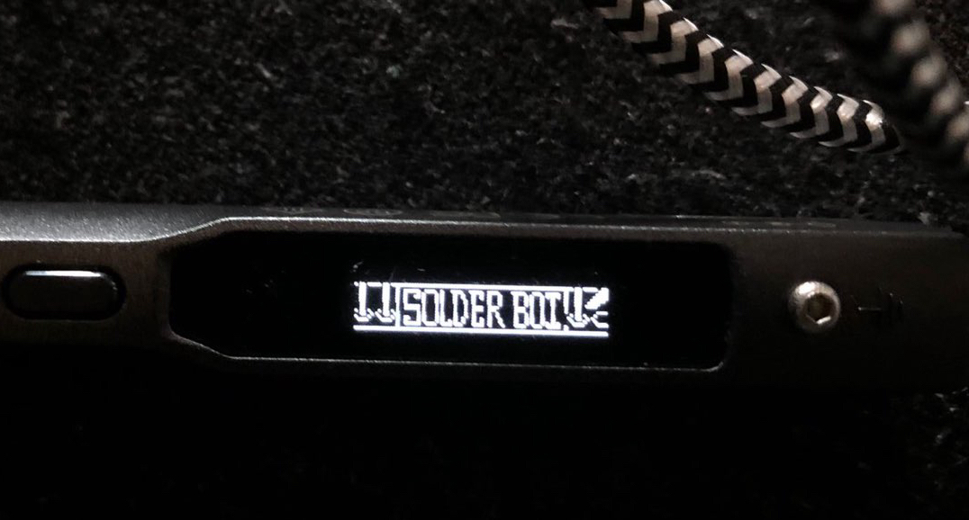An image of a TS100 soldering iron showing a custom bootscreen that says 'solder boy'.