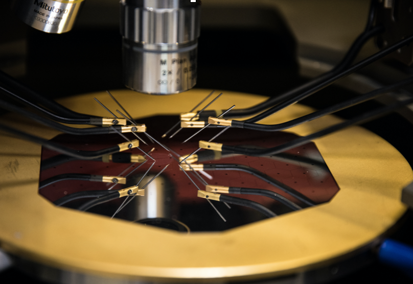 An image of test probes touching a silicon wager etched with hexagons